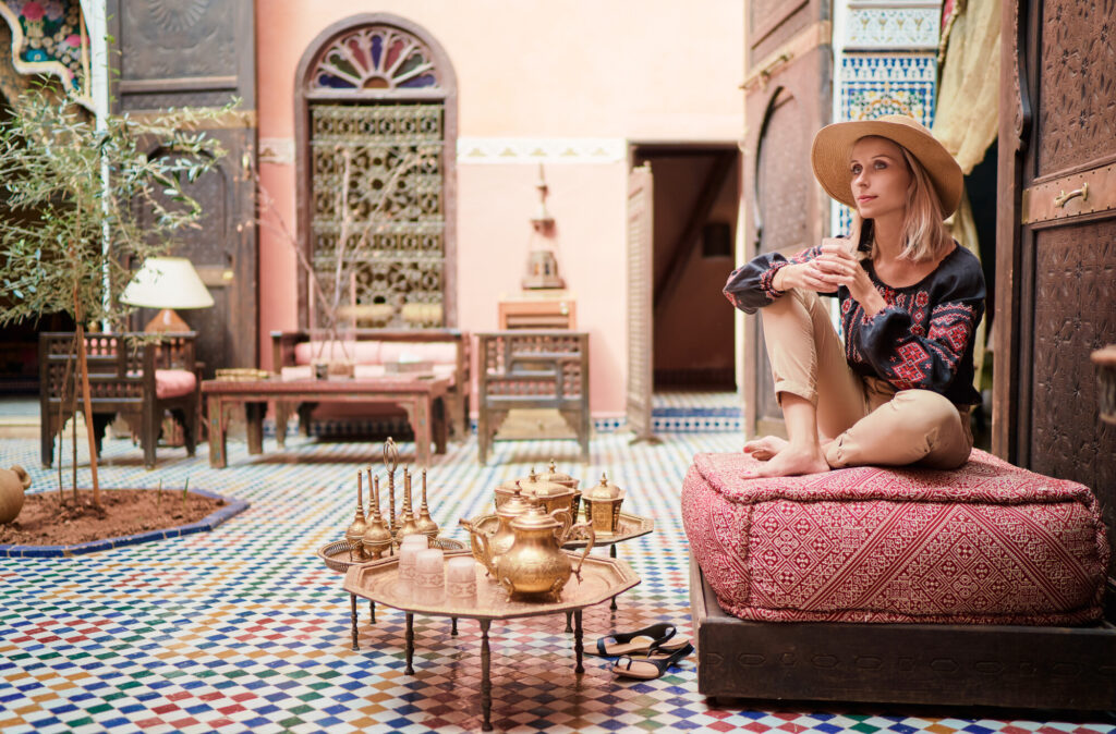 Jeune femme heureuse avec un chapeau se relaxant dans un intérieur de riad traditionnel dans la médina au Maroc